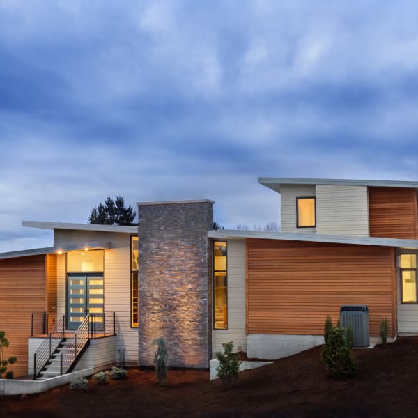 A modern house with horizontal wood siding and a stone chimney at dusk