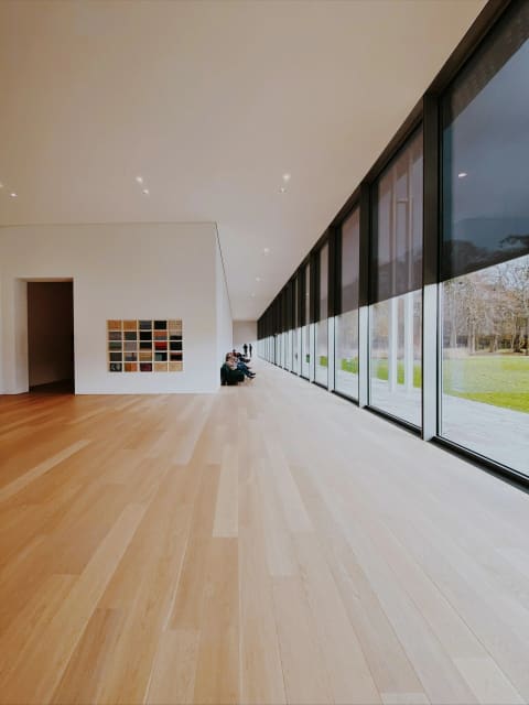 A long room with a light hardwood floor and floor-to-ceiling windows